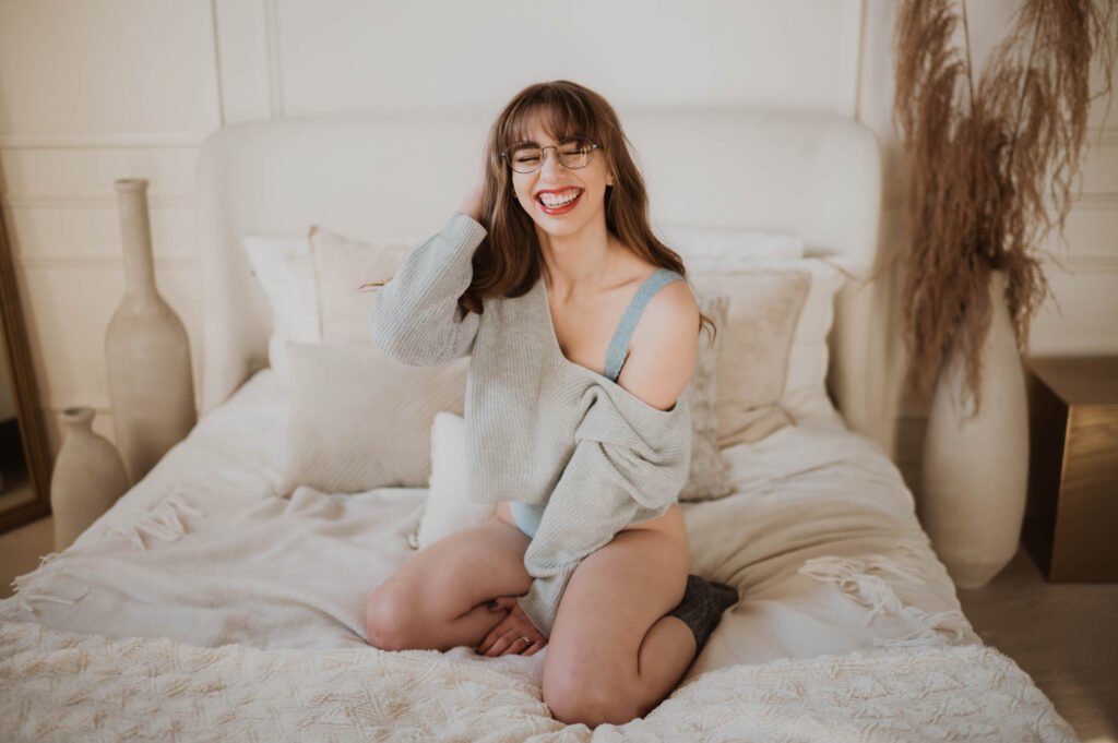 A woman is pictured on a bed wearing glasses and laughing