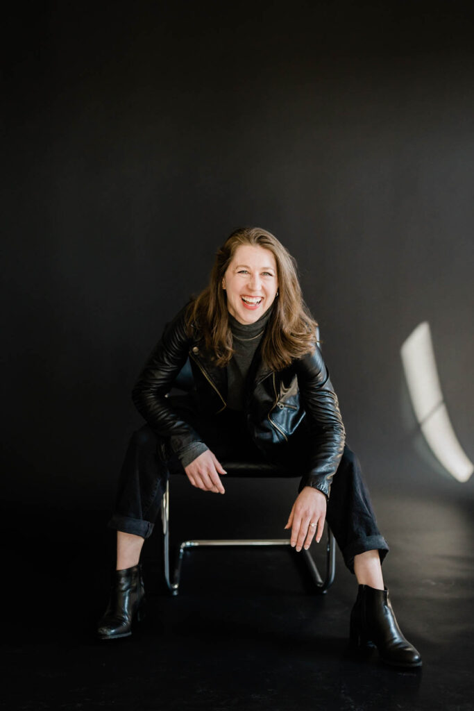 A woman is laughing as her picture is taking in black clothing in a boudoir studio