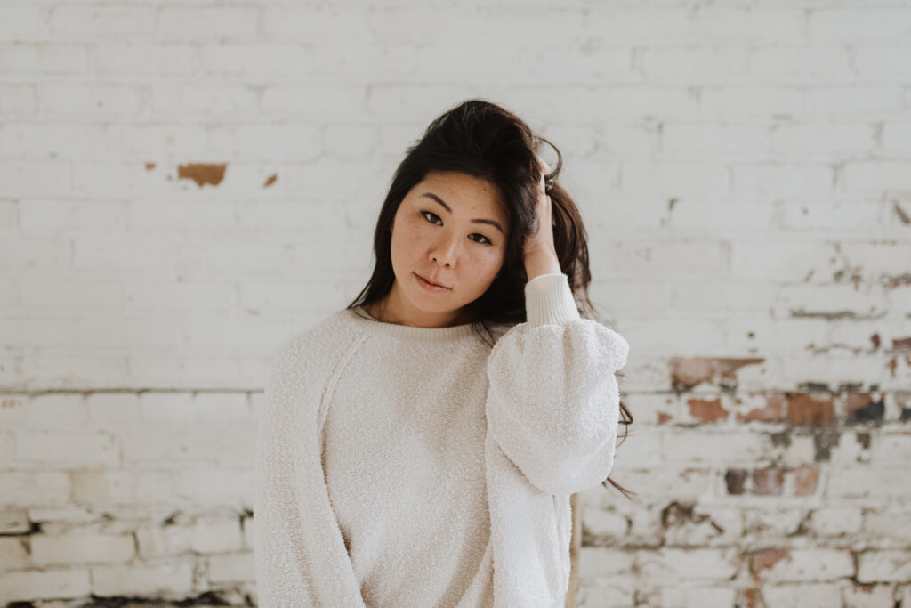 A woman poses in an oversized white long-sleeved shirt for a boudoir photography session