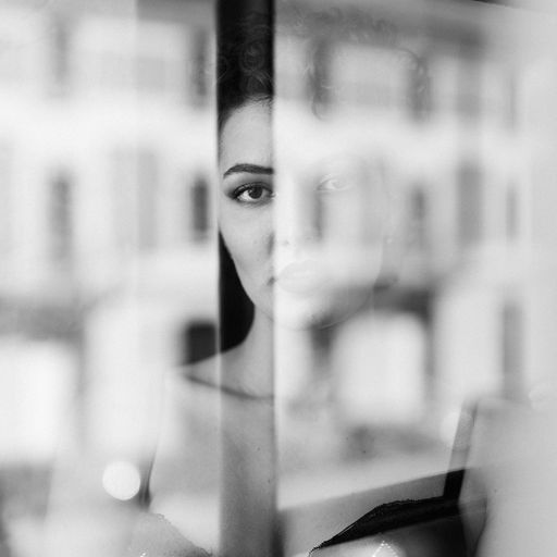 A woman poses through a glass window during a boudoir session